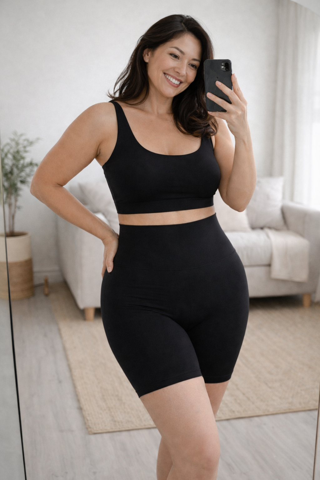 Woman taking a mirror selfie wearing the Vellomi black PostureLift shaping shorts and matching top in a home setting.